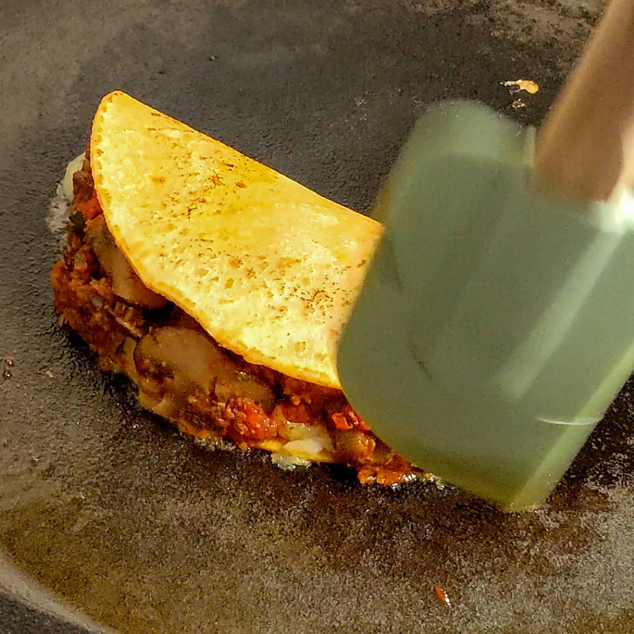 spatula tucking in the filling of the birria taco.